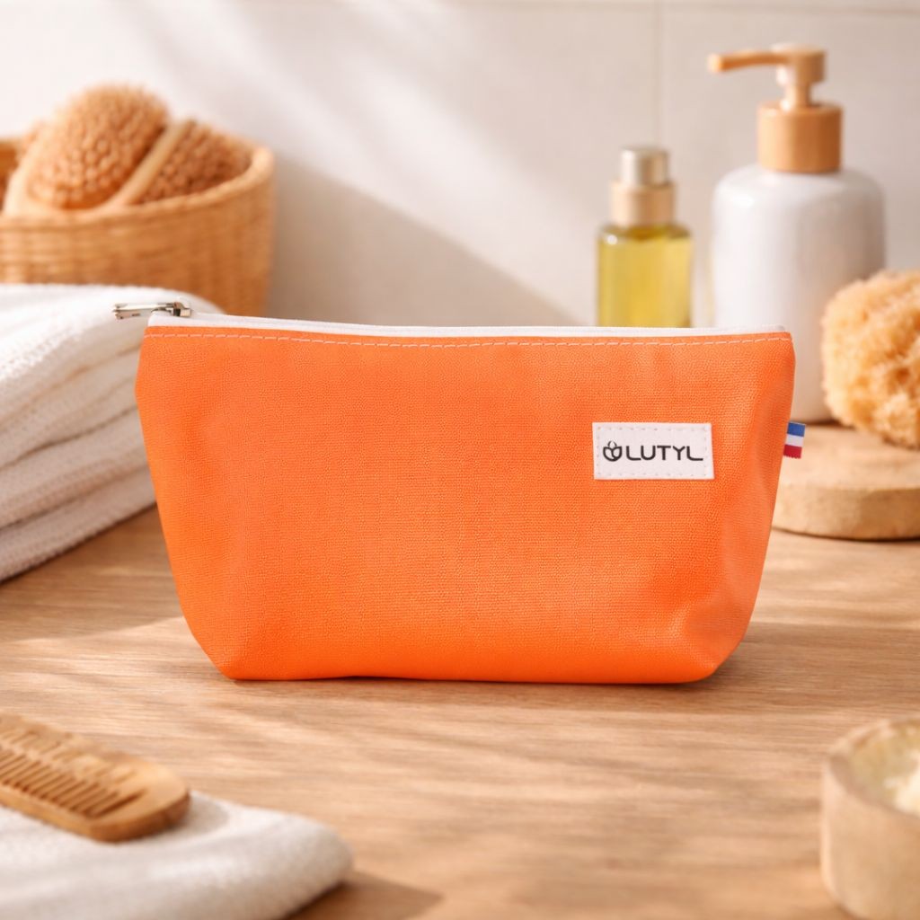 Trousse compacte corail Lutyl en toile enduite posée sur un meuble de salle de bain avec accessoires de toilette