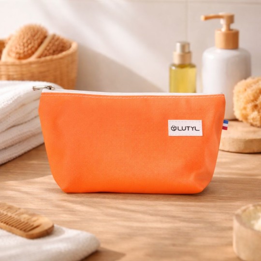 Trousse compacte corail Lutyl en toile enduite posée sur un meuble de salle de bain avec accessoires de toilette
