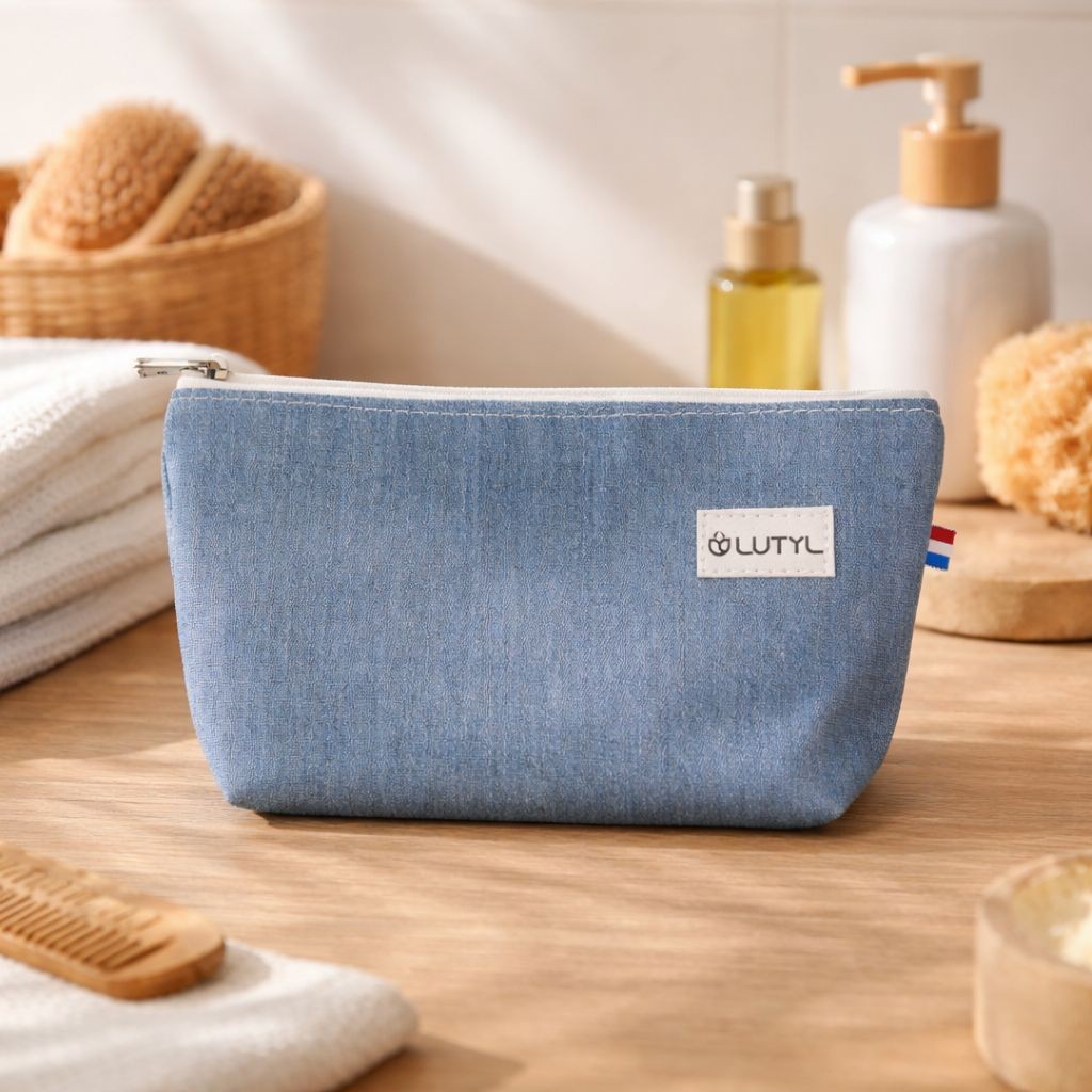 Trousse compacte bleu denim Lutyl en toile enduite posée sur un meuble de salle de bain avec accessoires de toilette