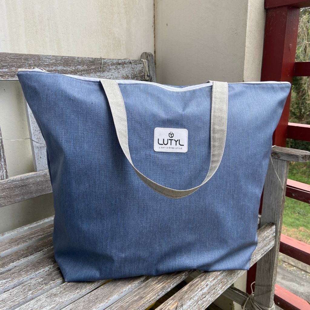 Sac zippé XL Lutyl bleu denim en toile enduite posé sur banc extérieur